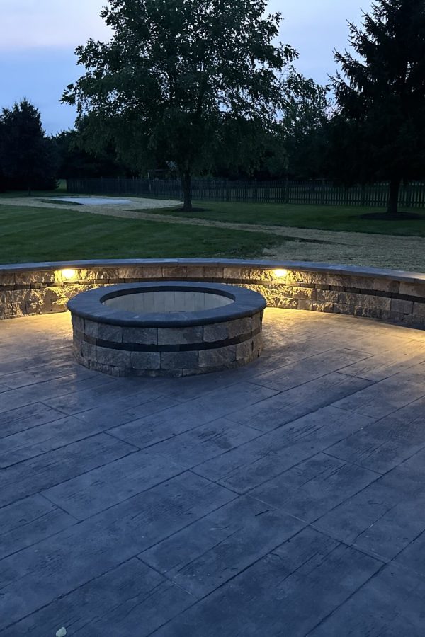 A cozy backyard fire feature with a circular fieldstone border and low-voltage landscape lighting for a rustic Illinois lakeside home.